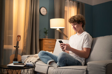 A bored young boy, teenager, schoolboy, student is relaxing on the couch in the evening with his...