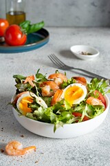 Fresh crispy salad with vegetables and seafood (shrimps) in a white plate on a light background. Healthy food concept.