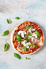 Cooking Italian pizza with tomato sauce, fresh tomatoes, cheese, mushrooms, salami slices and basil . Fresh food cooking concept at home. Semi-finished product, raw dough, step by step cooking.
