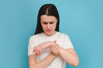 Young female massaging hand suffering from joint pain, isolated on blue background wall. Girl...