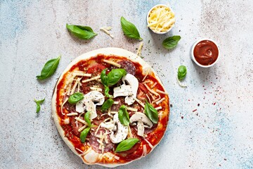 Cooking Italian pizza with tomato sauce, fresh tomatoes, cheese, mushrooms, salami slices and basil . Fresh food cooking concept at home. Semi-finished product, raw dough, step by step cooking.
