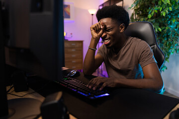 Professional pro video gamer playing on computer lost round in the game, he is heartbroken, disappointed, ashamed, the man covers face with hand, the room lit with led neon lights © ABCreative