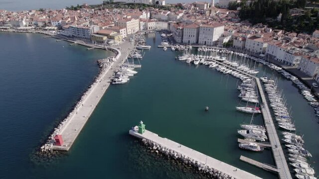 Descriptive panning drone video over the city of Piran in Slovenia, you can see the port with the boats in the water as the main part and the church in the background.