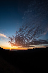 Orange cirrus clouds on a blue sunrise landscape form the top of a mountain