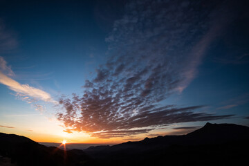 Orange cirrus clouds on a blue sunrise landscape form the top of a mountain