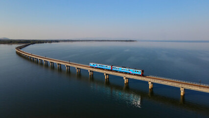Fototapeta na wymiar Motion blur of Train is running at high speed on a floating railway bridge. Aerial view of Train look like floating on the lake of Pa Sak Jolasid dam with blue sky at Lopburi province amazing Thailand