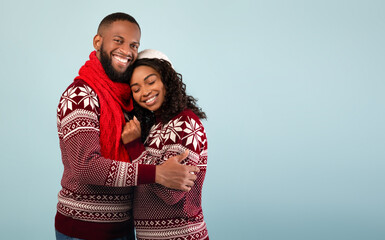 Affectionate african american spouses in Christmas sweaters embracing, standing over blue background, empty space