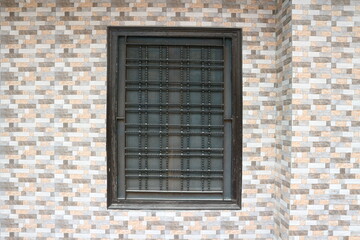 Brown window with bars and mesh. A dark window on a tiled wall.