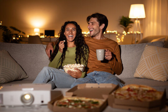 Cheerful Couple Using Home Cinema Projector Watching Comedy Movie Indoors