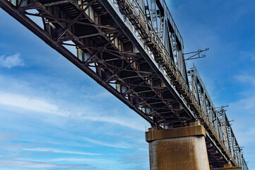 Bottom view of the railway bridge against the blue sky. Railroad bridge. Iranport crossing. Industrial design. Blue sky with white clouds. Railroad tracks. Iron structure on concrete supports.