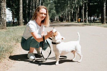 Young caucasian woman with dog on walk in park on sunny summer day. Owner and jack russell terrier puppy together outdoors