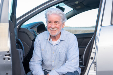 Attractive adult old senior man white haired sitting in his parked car smiling and looking away. Relaxed elderly grandfather enjoying drive