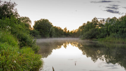 Evening on a river, trees reflection in water. Fog on the forest river