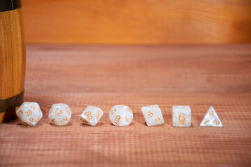 Set of role playing white dices lie in a row near light stylized beer mugs on a gaming table made of wood: background for role-playing games with place for text, side view