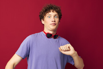 guy with red curly hair guy in a purple t-shirt with sunglasses posing red background