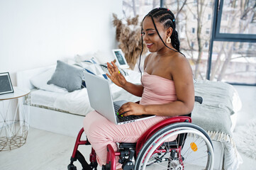 Young disabled African American woman in wheelchair at home working with laptop.