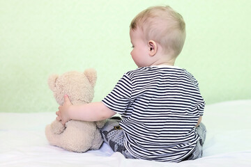 A defocused baby sits next to his toy, teddy bear. Early socialization. Lonely child waiting for parents. Copy space - concept of children's love, care, fidelity, friendships, communication