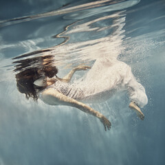 A girl in a white dress with dark hair swims underwater as if flying