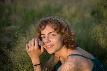 face of a teenage girl sitting in tall grass enjoys nature and relaxation. Nice young woman is resting in the park. spring, summer, sunbathing. dreams, harmony, replenishment of vitality. earth day