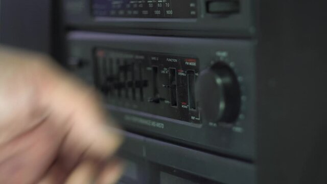 A man's hand moves the switches on the tape recorder. Mode setting. Analog control. Equalizer. Dark body. Old tape recorder. Close-up. Fragment of an object