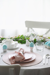 Easter table setting with blue coloful eggs, festive decorations, fresh flowers. Elegance dinner at home interior. Close up.