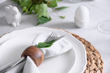 Easter table setting with yellow chick, festive decorations, fresh flowers and eggs on white tablecloth. Elegance dinner at home. Close up.
