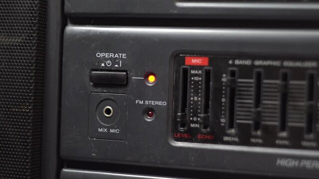 Turning on the power button on the cassette recorder. Dark body. Old tape recorder. Red LED. Close-up. Man's hand.