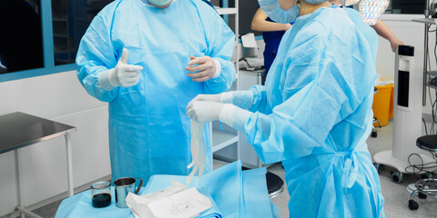 Doctors in surgical uniforms wear sterile gloves before starting surgery.