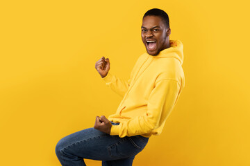 Emotional Black Man Shaking Fists In Joy Over Yellow Background