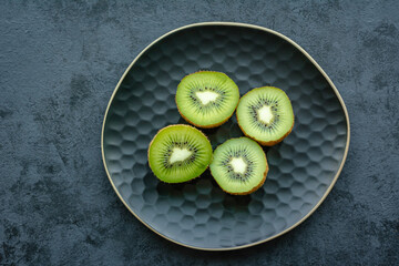 Fresh juicy kiwi fruit on a plate. Dark background - obrazy, fototapety, plakaty