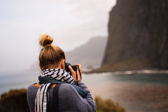 Back of a blonde woman taking photos of the cliffs and ocean