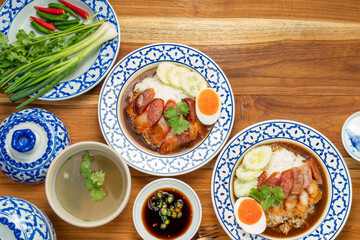 Rice with red roasted pork, Crispy Pork with sauce and Egg topped in a white dish on wooden table.