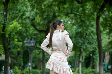 Outdoor portrait of gorgeous young woman with long ponytail in elegant satin dress in city park