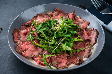 Marbled beef carpaccio with arugula and parmesan cheese. Black background