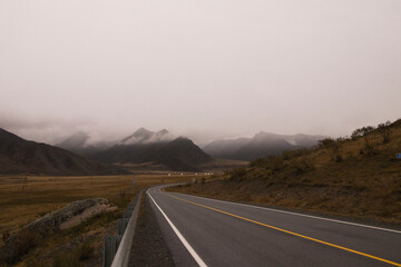 Fototapeta premium Beautiful road in the mountains, late autumn . The peaks of the mountains are covered with fog. Altai.