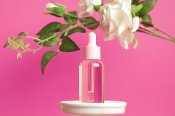Glass dropper bottle on podium with flowers on pink background. Cosmetic container mock-up. Background for branding and packaging presentation. Natural skincare beauty product concept