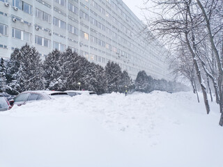 City after snowfall and blizzard. Cars covered with snow up to the very roof are parked on a...