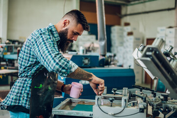 Male worker pressing ink on frame while using the printing machine in a workshop