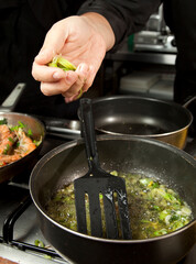 A chef frying chopped spring onion in a pot, about to put in some more.