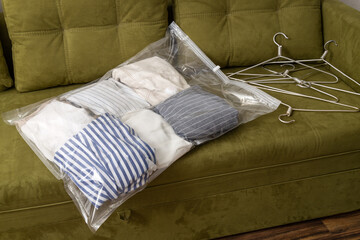 Vacuum bag for clothes and empty hangers on the green sofa indoor.Apparel storage
