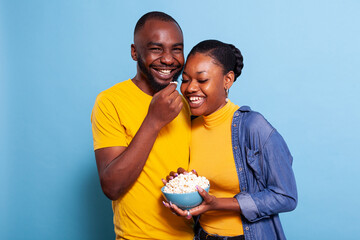 Amused people watching comedy on television and having snack over blue background. Cheerful couple...