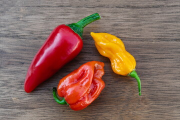 Three fresh organic red, orange and yellow hot chili peppers on a wooden table
