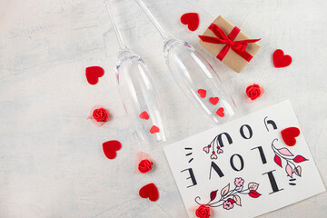 top view of two champagne glasses with red hearts, gift with ribbon and valentine with words I love you. concept of holiday, congratulations, valentine's day, engagement, wedding, anniversary. flatlay