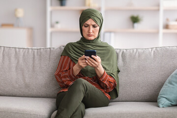 Serious Muslim Woman Using Smartphone Frowning Reading News At Home