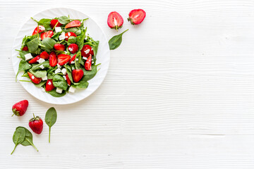 Green spinach salad with red strawberry and goat cheese, top view