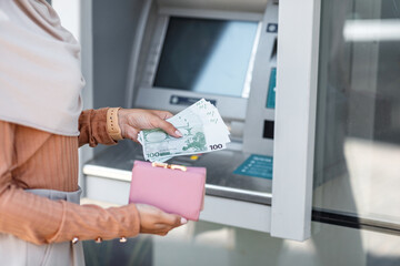 Millennial unrecognizable arab muslim female in hijab withdraw money, put euro in wallet near ATM