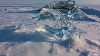 Transparent shiny shards of natural ice. Close-up. The glare of the sun on the edges, shadows on the snow. Frozen Lake Baikal