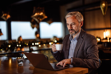 Thoughtful caucasian novelist, writing his story on laptop, while having coffee at a bar.