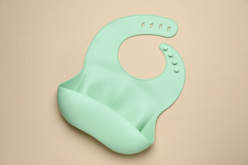 Green silicone baby bib on beige background, top view. First food