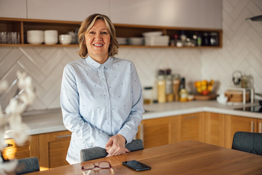 Portrait of happy middle-aged woman, standing tall behind the kitchen table.